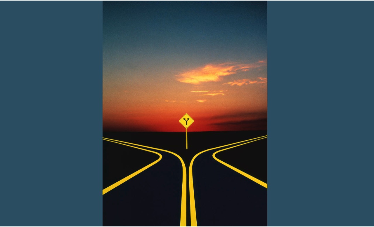 Two diverging roads at sunset with a yellow road sign indicating a fork ahead.