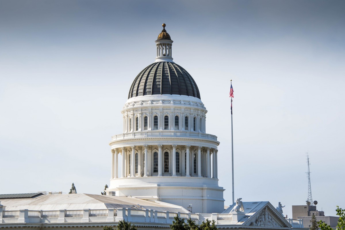 The dome of a white government building with an American flag flying nearby